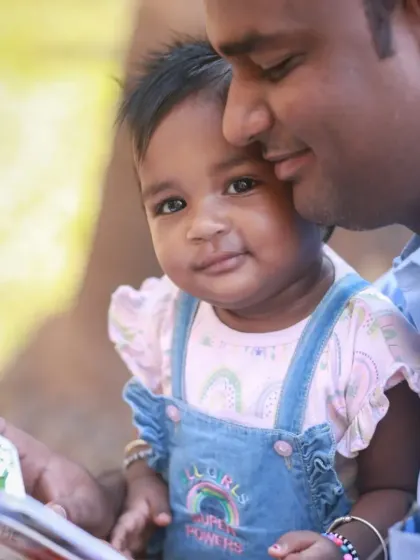 A sweet father-daughter moment during an outdoor shoot, with the baby looking curiously at the camera while cuddled in her dad's arms.