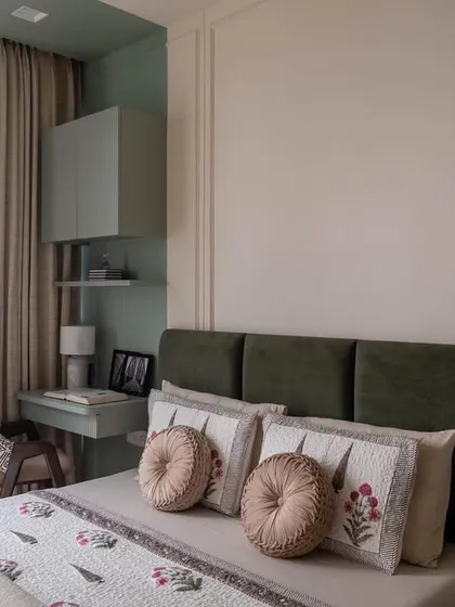 The 'after' shot of the guest bedroom. The combination of a dark green headboard with soft-toned bedding and a compact study desk creates a welcoming and functional space.