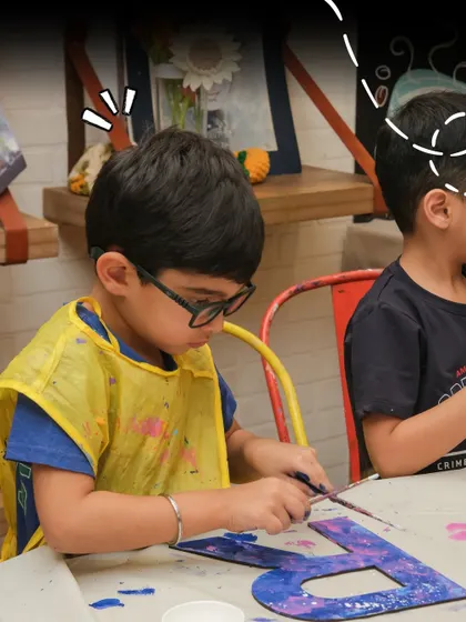 A young boy wearing a yellow apron concentrates on painting a large letter 'B' during a fun and crafty birthday celebration.