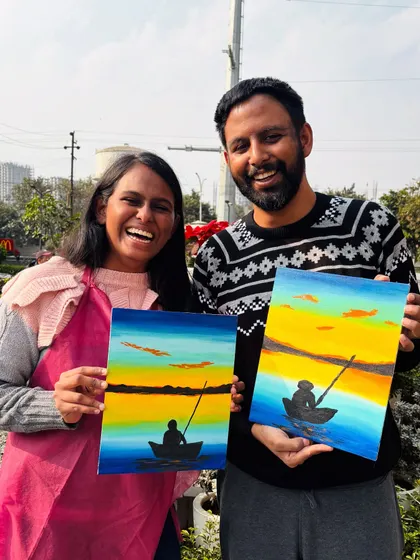 A couple showing off their matching sunset-over-the-water paintings. A perfect result from a relaxing and romantic paint date.