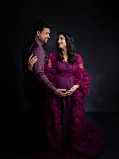 An intimate couple's pose during a maternity shoot. The dark, moody lighting and the rich color of the gown create a romantic and sophisticated portrait for the expecting parents.