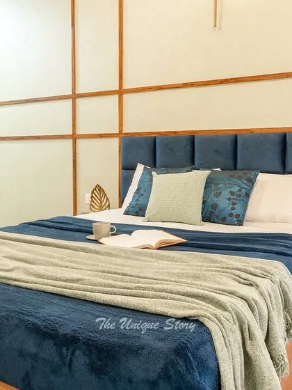 A cozy bed with a bold navy blue tufted headboard set against a wall with geometric wood paneling. The mix of textures and the warm wooden bed frame create a comfortable and stylish sleeping area.