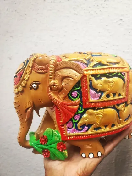 A side view of another hand-painted wooden elephant, showing the detailed carvings of smaller elephants along its body.
