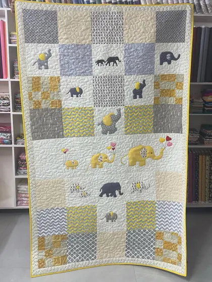 This charming baby quilt is covered in sweet appliqué elephants in shades of yellow and grey. Some elephants even hold heart-shaped balloons, adding a touch of whimsy.