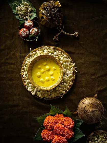 A moody, artistic flatlay of Diwali sweets and flowers, using shadows and rich colors to create a dramatic effect.