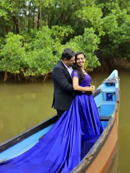 A dramatic pre-wedding photo of a couple in a boat, with the bride's vibrant blue gown trailing in the water.