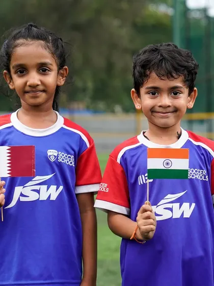 A boy and a girl stand together with the flags of India and Qatar, symbolizing our commitment to unity and equal opportunities in football.