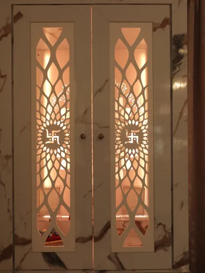 This mandir is set within a marble-finish cabinet, with intricate CNC-cut doors. The internal lighting highlights the deities and creates a warm, inviting glow.