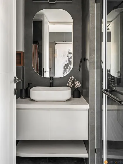 A sophisticated bathroom with a monochrome palette of black and grey. The floating white vanity and oval mirror create a clean, minimalist look, while the dark tiles add a sense of drama.