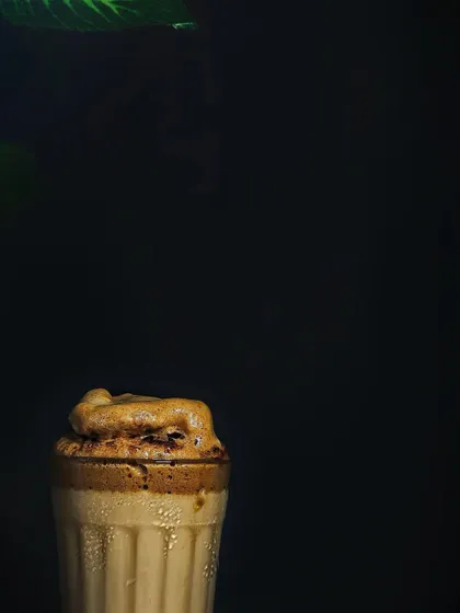 A minimalist shot of a Dalgona coffee against a stark black background. This high-contrast, moody style emphasizes the drink's form and texture, giving it a sophisticated look.