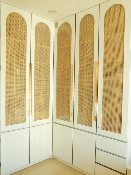 This custom L-shaped wardrobe features arched rattan panels, providing ample storage while adding a chic, airy feel to the master bedroom.