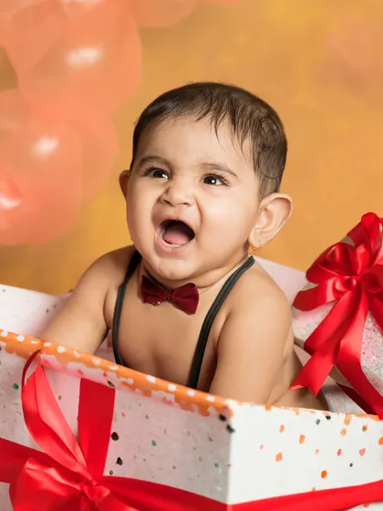 A baby boy in a gift box, wearing a bow tie and roaring with laughter. A fun and creative way to capture a milestone.