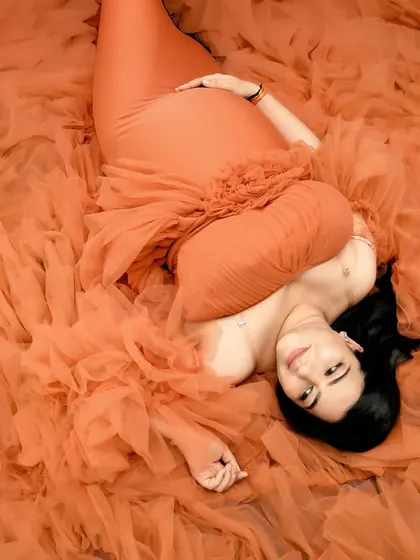 A unique top-down angle showing the mom-to-be lying in a sea of orange tulle from her gown. This artistic shot focuses on texture, color, and serene expression.
