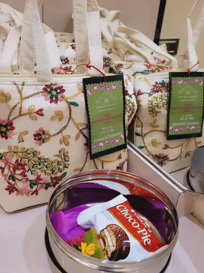 For a gift that is both beautiful and practical, I offer these hand-embroidered tote bags. This set was created for a gruhapravesha and included a stainless steel box with treats, showing how we can mix traditional and modern elements.