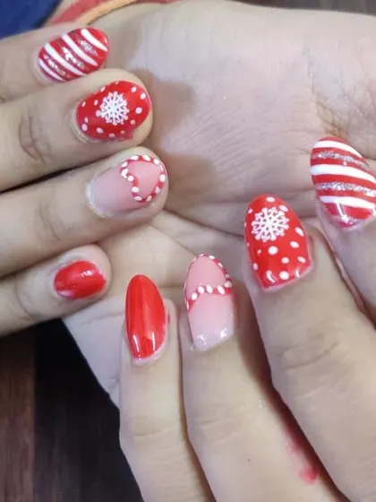 A festive Christmas-themed manicure with hand-painted snowflakes, candy cane stripes, and polka dots in red and white.