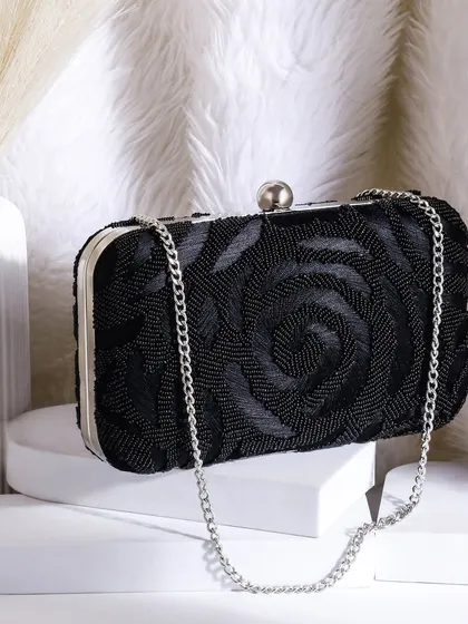 A chic and modern shot of a black floral beaded clutch. The clean white props and fluffy background create a sophisticated and stylish composition.