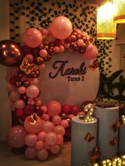 A close-up of a butterfly-themed birthday decor. This image highlights the rose gold and pink balloon garland, illuminated name, and butterfly details on the pedestals.