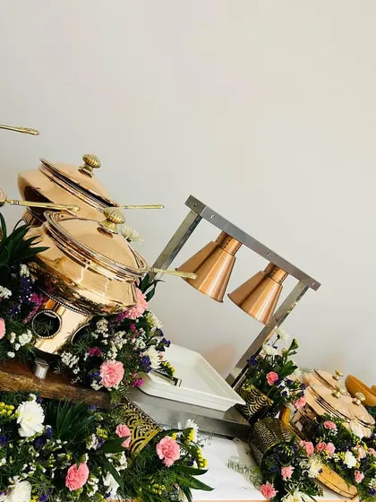 A close-up of our copper chafing dishes and food warmers surrounded by lush arrangements of pink, purple, and white flowers, perfect for an intimate celebration.