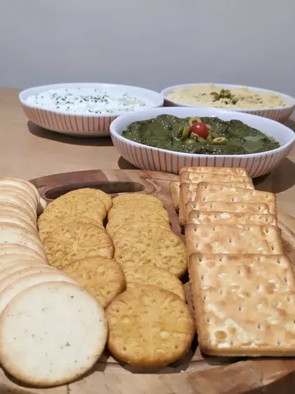 A trio of house-made dips served with a variety of crackers. This setup offers guests a selection of flavors, including a green herb dip, hummus, and a creamy yogurt-based dip.