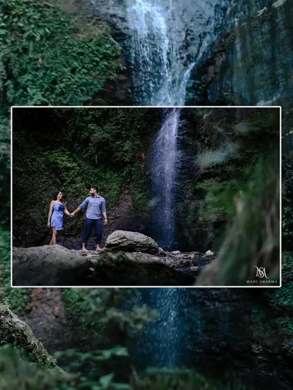 A wide shot showing the scale and beauty of the waterfall, with the couple standing together in nature.