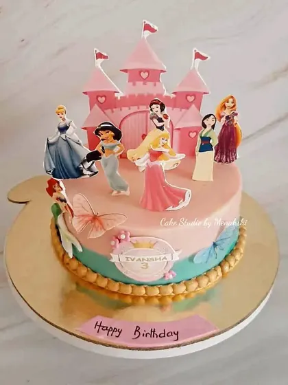 A Disney princess themed cake for a 3rd birthday. This design features a pink castle and a lineup of beloved princesses like Ariel, Cinderella, and Snow White.
