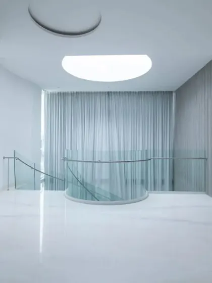 A serene, minimalist space featuring a circular skylight and floor-to-ceiling grey curtains, demonstrating how emptiness and light can be used to create a sense of calm and inertia.