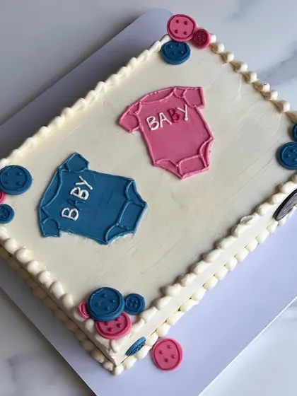 A simple and sweet sheet cake for a baby shower. Sheet cakes are perfect for larger gatherings because they are easy to cut and serve, ensuring everyone gets a piece. This one is decorated with cute pink and blue baby onesies.