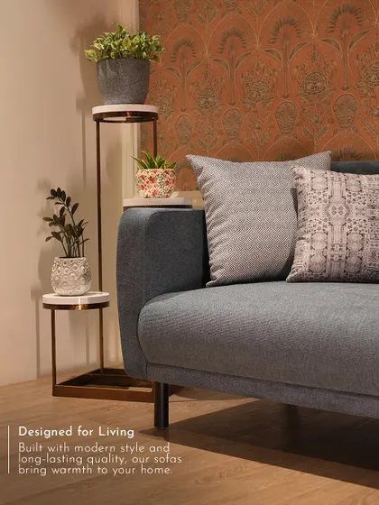 This modern grey sofa is styled with complementary cushions and a sleek plant stand, showing how my furniture serves as a foundation for a warm and inviting home.