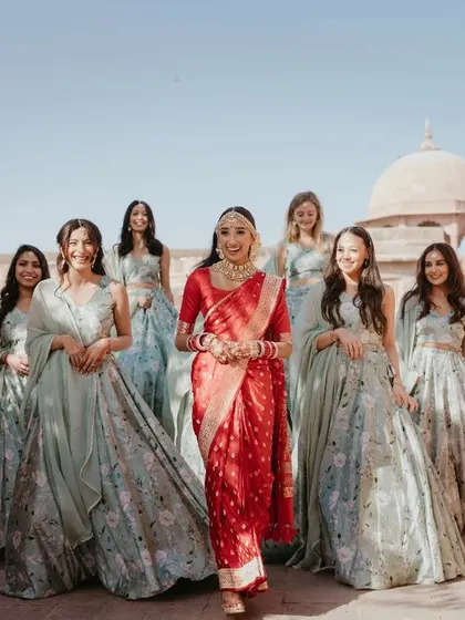 The bride's grand entrance with her entire bride tribe. This wide shot captures the joy and camaraderie, with the beautiful palace architecture providing a stunning backdrop.