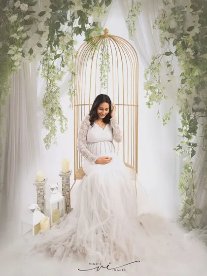 Seated in a golden birdcage chair adorned with white wisteria, this mother-to-be looks like she's in a secret garden, creating a whimsical and romantic portrait.
