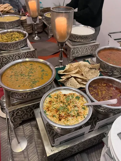 A classic Indian buffet featuring comforting dishes like dal, boondi raita, and assorted curries served in traditional, ornate serveware. This spread is a tribute to the rich, timeless flavors of Indian home cooking.