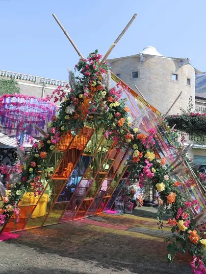 The entrance for a modern Haldi, featuring a triangular arch made of colorful glass panels and adorned with flowers. This creates a unique and artistic first impression.
