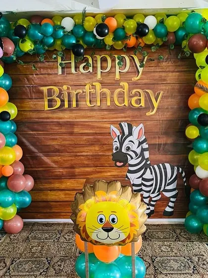 A jungle-themed birthday party with a wood-panel-print backdrop. The setup is decorated with a balloon arch and various animal foil balloons.