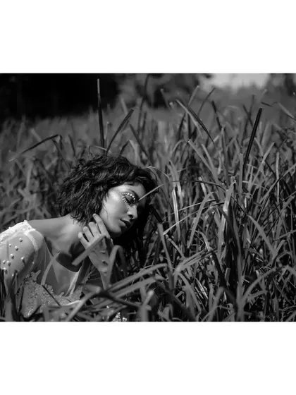 A dreamy and ethereal black and white portrait. The model, nestled in the grass with eyes closed, looks peaceful and connected to nature.
