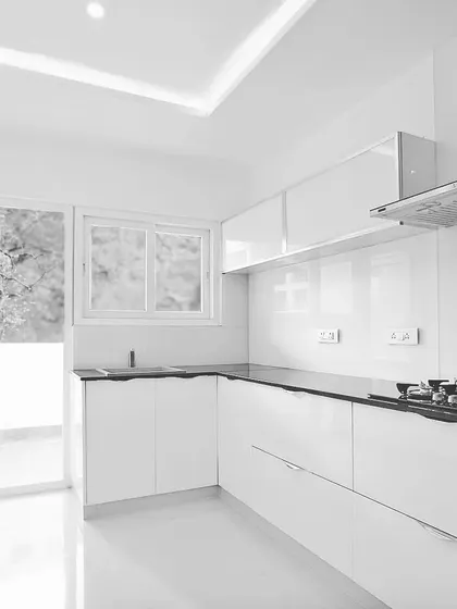 A minimalist and highly functional kitchen design. This space features handleless white cabinets, a contrasting black countertop, and a chimney, all arranged for a clean look and an efficient workflow.