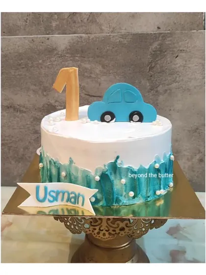 A simple and sweet first birthday cake with a car theme. The blue car topper and watercolor buttercream effect make it a charming choice for a little one's special day.