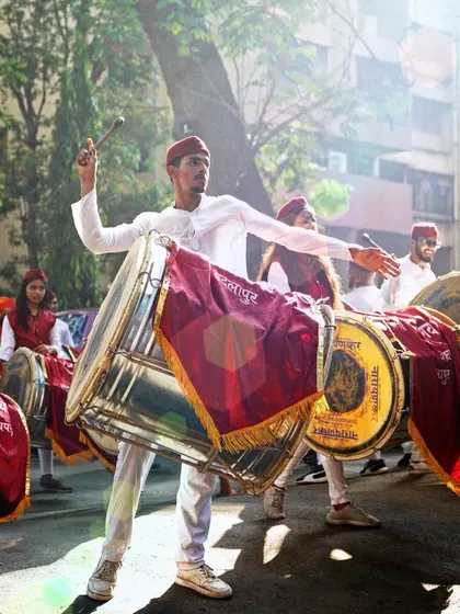 Backlit by the morning sun, a dhol player creates a powerful silhouette. This shot highlights the dramatic and athletic nature of the dhol-tasha performance during the Gudi Padwa parade.