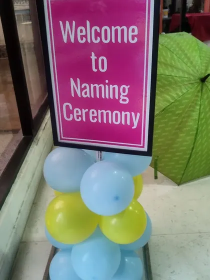 A simple 'Welcome to Naming Ceremony' sign with a small balloon arrangement.