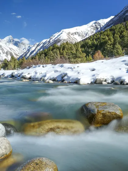 A series of photos capturing the serene beauty of a river flowing through a snow-lined valley. The long-exposure shot creates a milky effect on the water, contrasting with the sharp peaks.