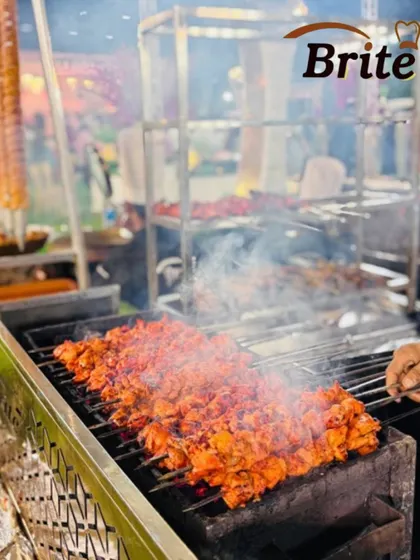 Skewers of bright red chicken tikka grilling over charcoal, filling the air with a smoky, aromatic scent.