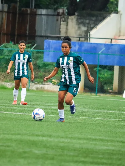 Dribbling with intent. A player advances the ball up the field, with a teammate providing support in the background.