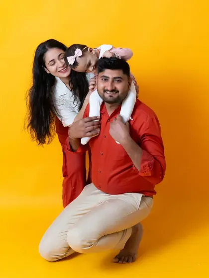 A playful family portrait against a bright yellow background. The dad gives his daughter a shoulder ride, creating a fun and dynamic image full of laughter.