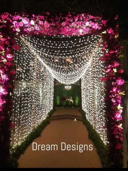 A tunnel of light makes for a truly grand entrance. This walkway is framed by a deep pink floral arch and walls of cascading fairy lights, leading guests into the reception in style.