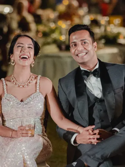 The bride and groom share a laugh while seated at their reception, enjoying the speeches and the company of their loved ones.