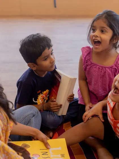 The pure excitement of storytime. Children react with wide-eyed wonder and laughter as they listen to an engaging tale, showing how reading together can be a lively, interactive experience.