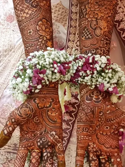 The rich henna stain beautifully complements the bride's floral jewelry and wedding attire. You can even see the name 'Sandeep' artfully hidden in the design on the palm.