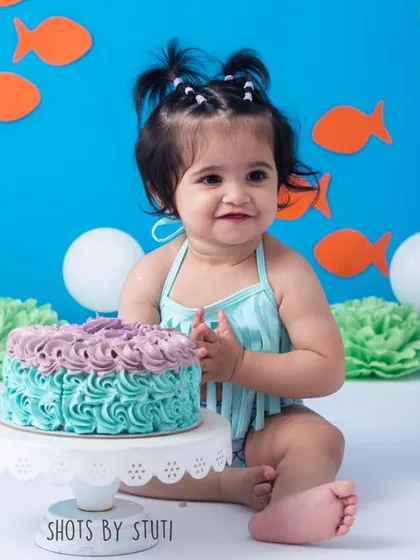 Clapping her hands in delight with a face full of cake. This is the kind of happy, messy moment that perfectly sums up the fun of a first birthday cake smash.