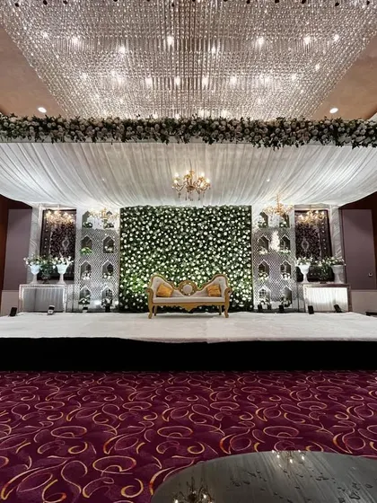 A wide-angle view of the grand white and green stage at Crowne Plaza. The scale of the floral arrangements and the massive crystal chandelier creates an atmosphere of pure luxury.