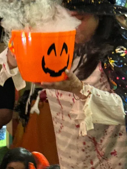 A host in a witch costume holds a smoking cauldron, delighting the children with a bit of spooky, interactive fun during the Halloween party.