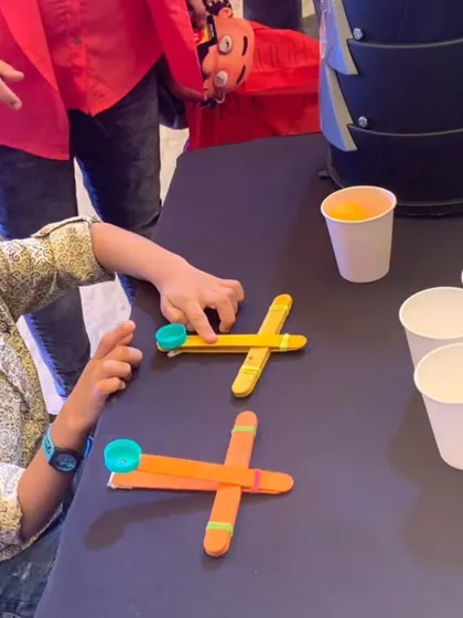 A young engineer makes adjustments to his catapult, getting ready to launch a projectile at a tower of cups. This activity teaches physics in a fun, hands-on way.
